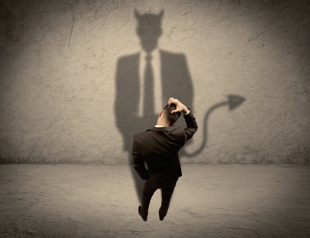 An experienced tricky businessman in suit looking at his devil desguise shadow reflected on the wall concept