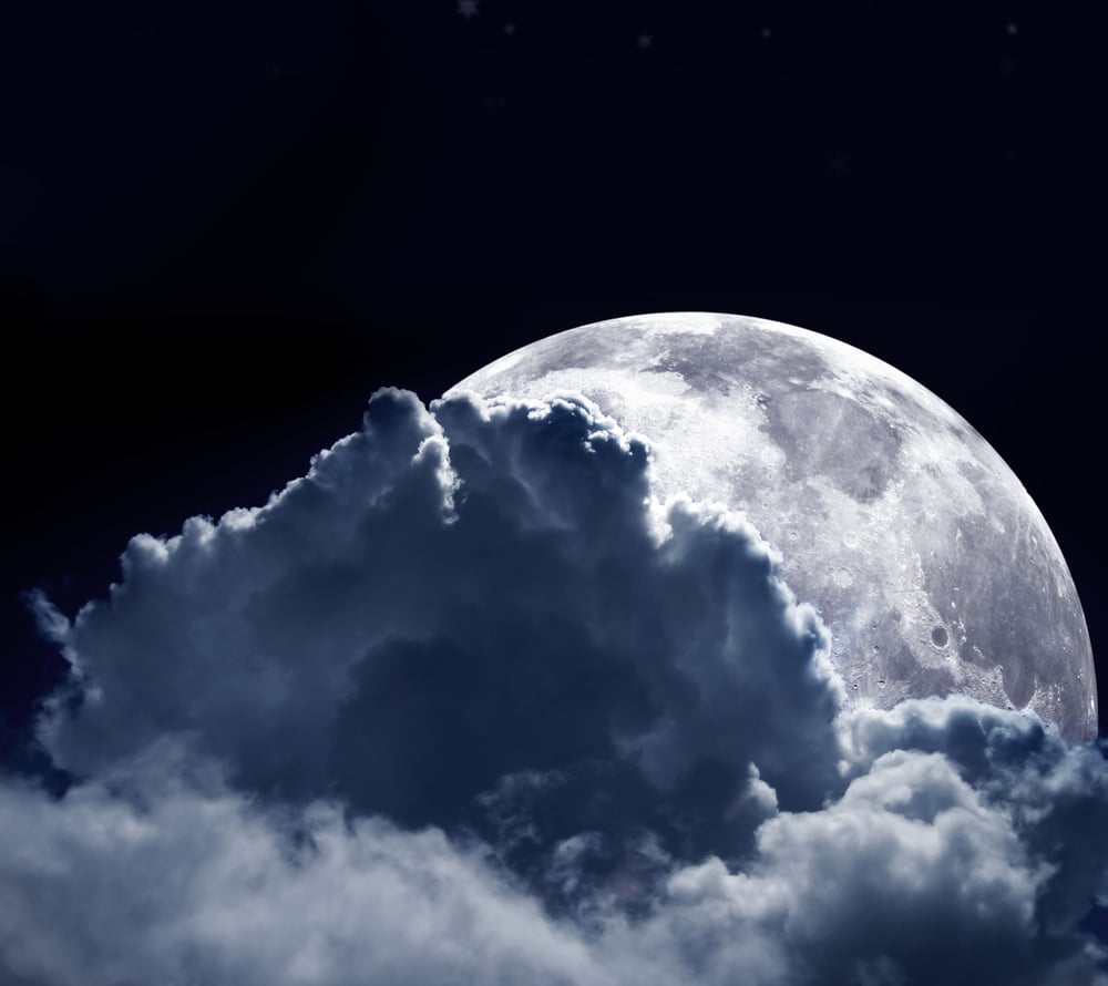 Beautiful shot of a full moon behind some clouds in a dark blue sky
