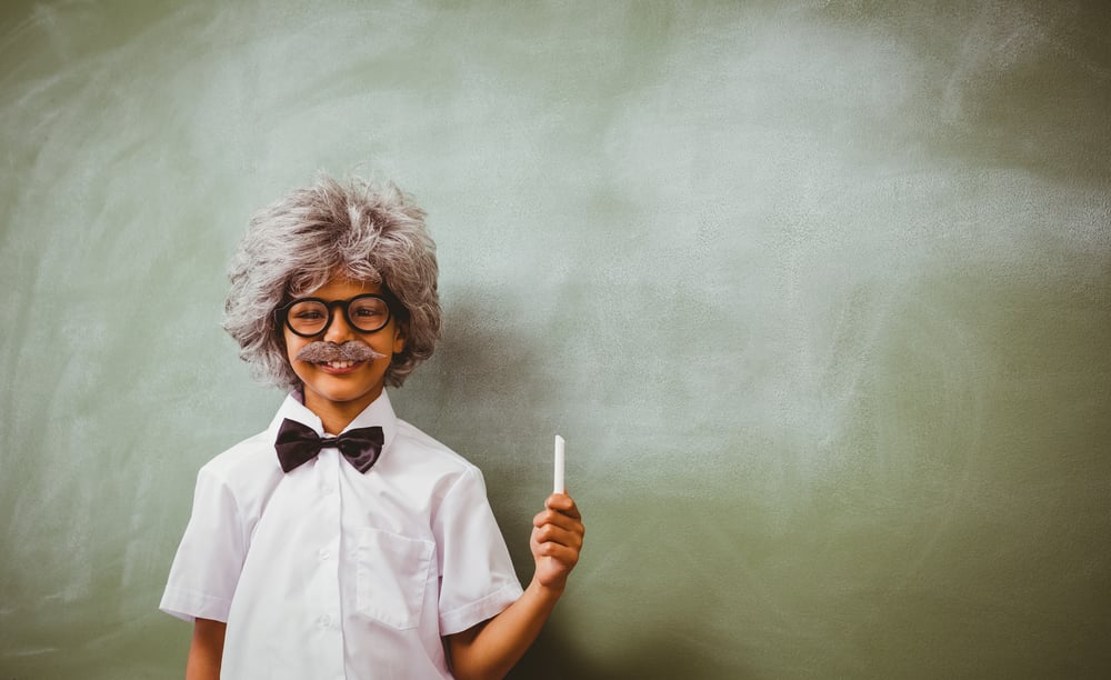 Portrait of little boy dressed as senior teacher in front of blackboard