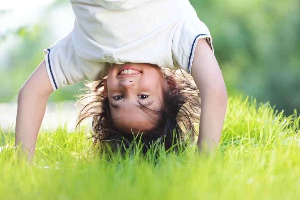 Portraits of happy kids playing upside down outdoors in summer park walking on hands