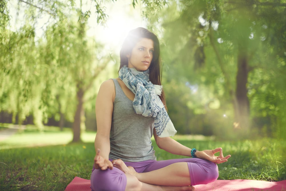 Serene and peaceful woman practicing mindful  awareness by meditating in nature with sun flare.