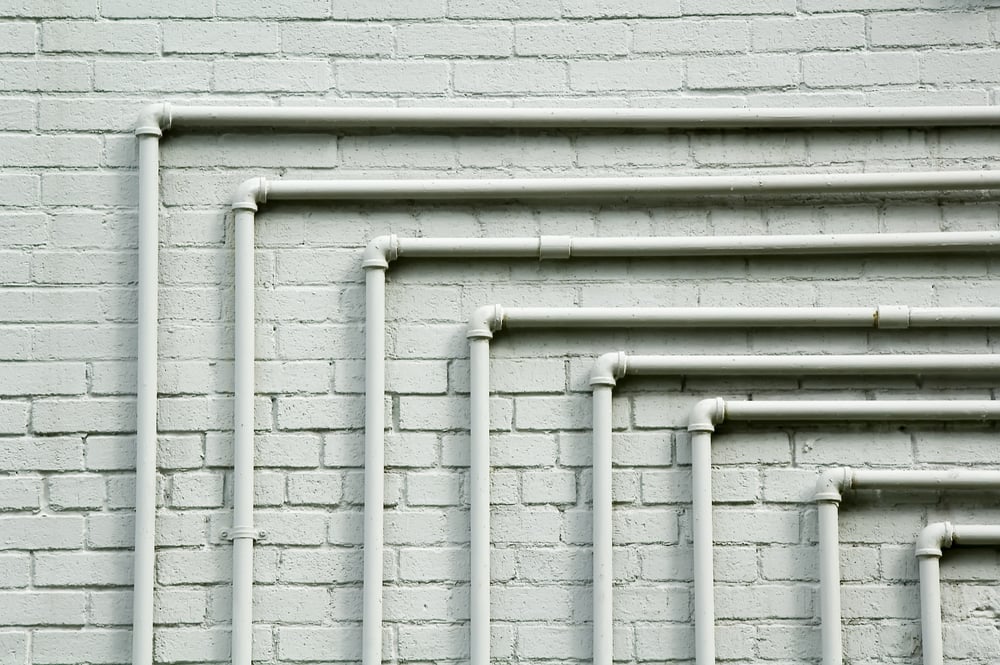Series of parallel pipes, each with 90-degree turn, along whitewashed brick wall