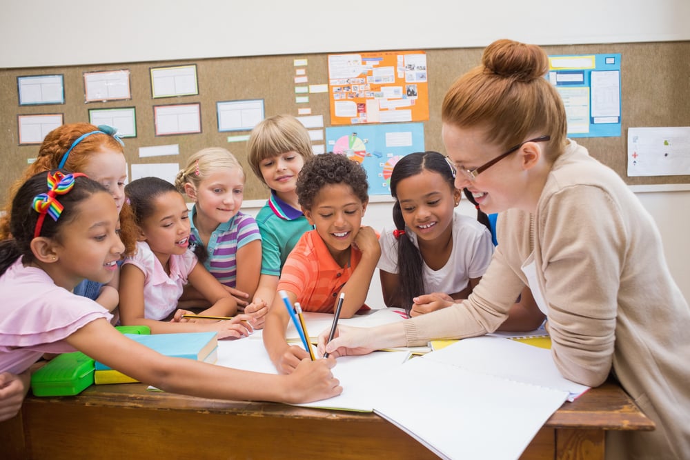 Teacher and pupils working at desk together at the elementary school-1