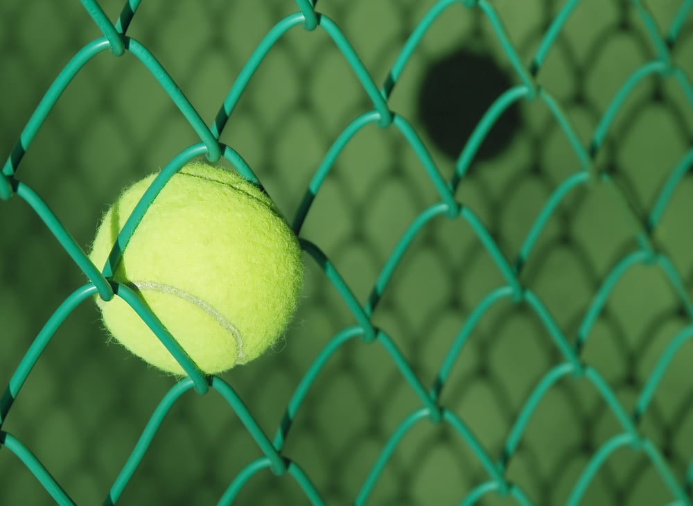 Tennis ball stuck in chain-link fence and shadows on tennis court
