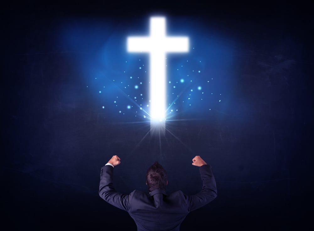 Young businessman standing and looking at a glowing cross above his head