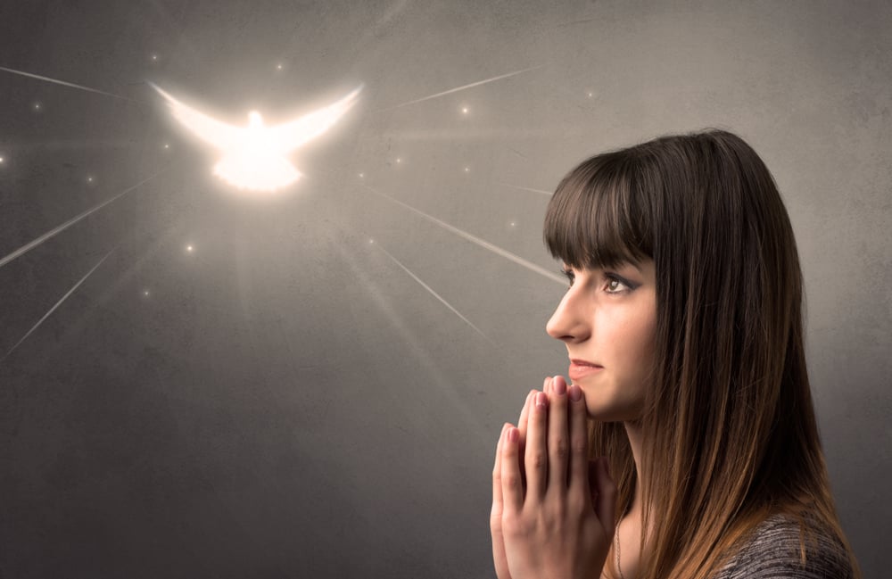 Young woman praying on a grey background with a sparkling bird above her